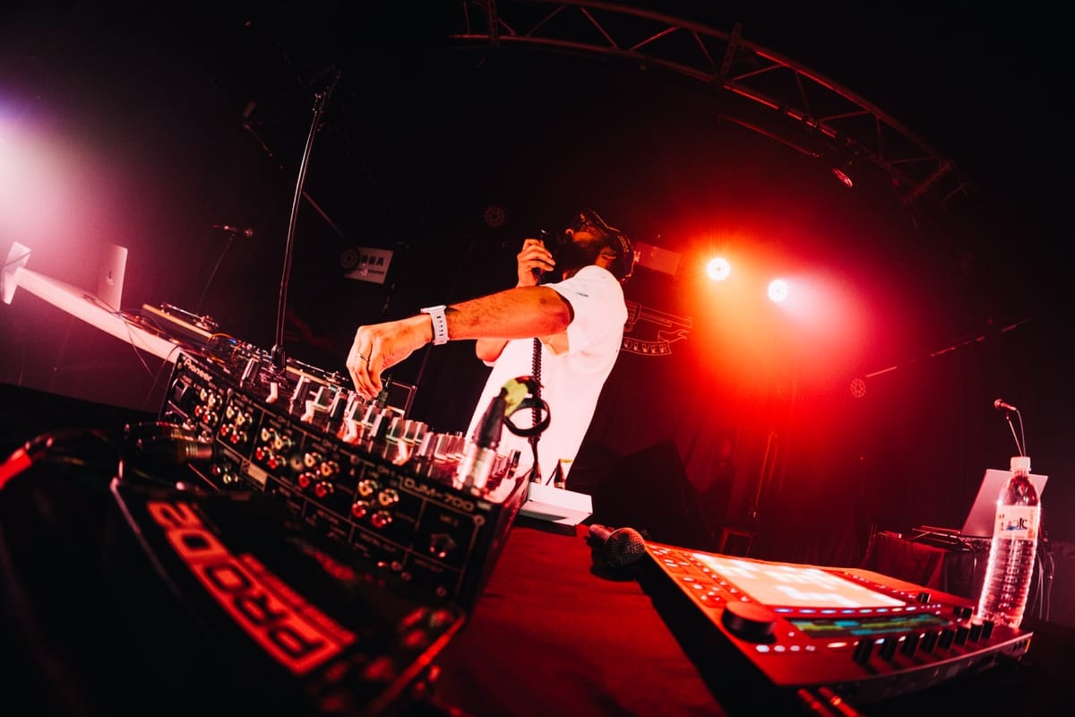 Fisheye photo of Paul adjusting controls on a mixer, while rapping into a mic